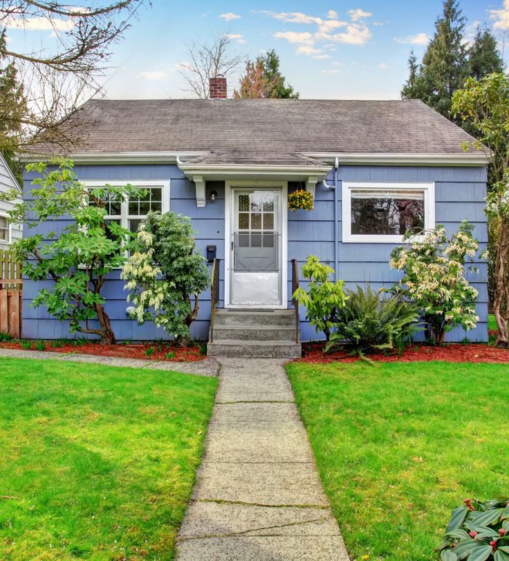 a blue house with green grass and trees in the front yard, on a sunny day