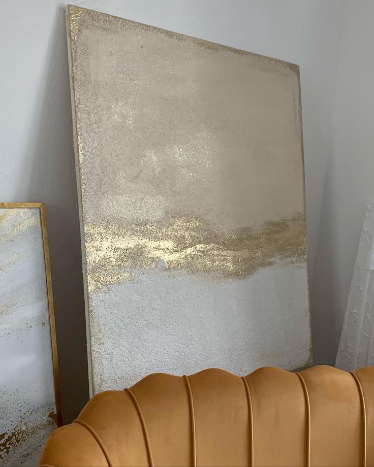 a gold and white painting sitting on top of a brown leather chair next to a wall