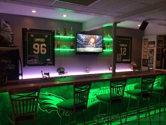 a sports themed bar with neon lights and green chairs in front of the bar area