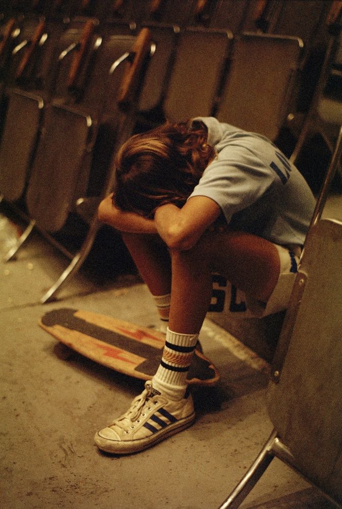 a person with their head down sitting on a skateboard in front of a row of chairs