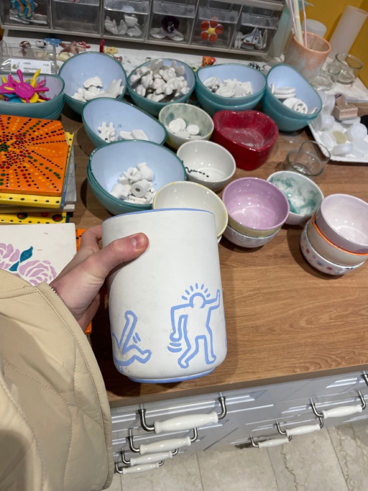 a person is holding a cup in front of bowls and other items on a table