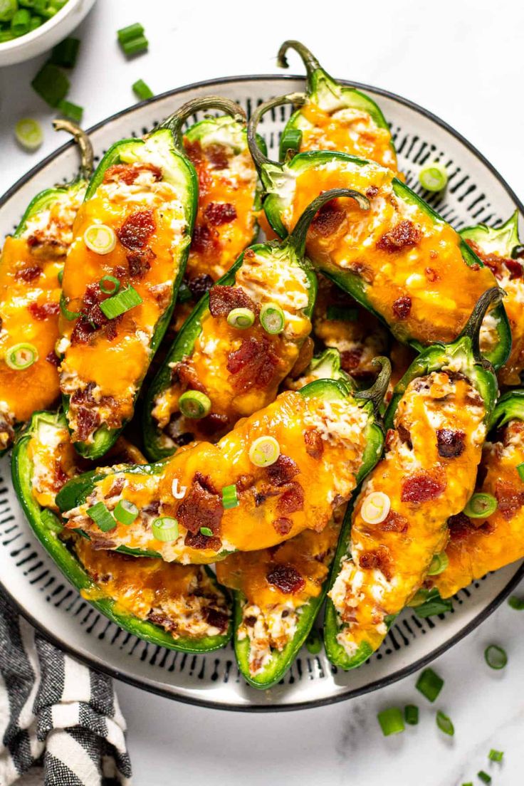 a white plate topped with green peppers covered in cheese and seasoning next to a bowl of greens