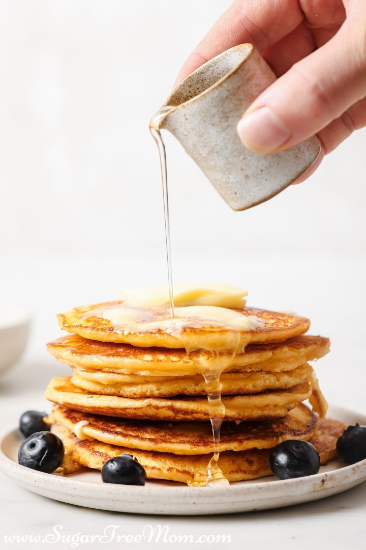 a stack of pancakes with syrup being drizzled over them and blueberries