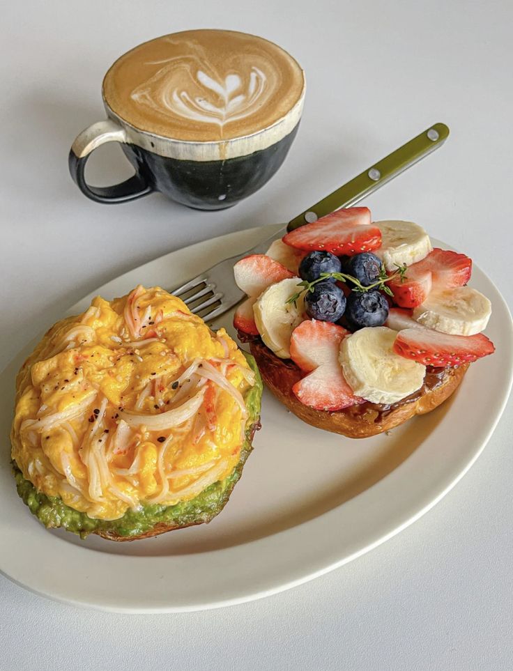 a white plate topped with a sandwich next to a cup of cappuccino