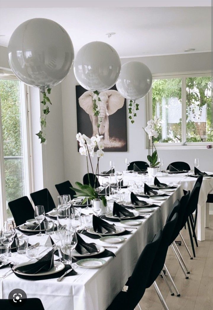 the table is set with black and white plates, silverware, and large balloons