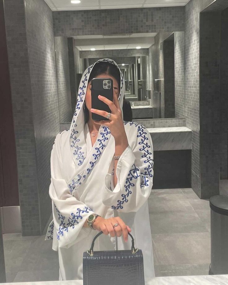 a woman taking a selfie with her cell phone in a hotel bathroom while wearing a white robe