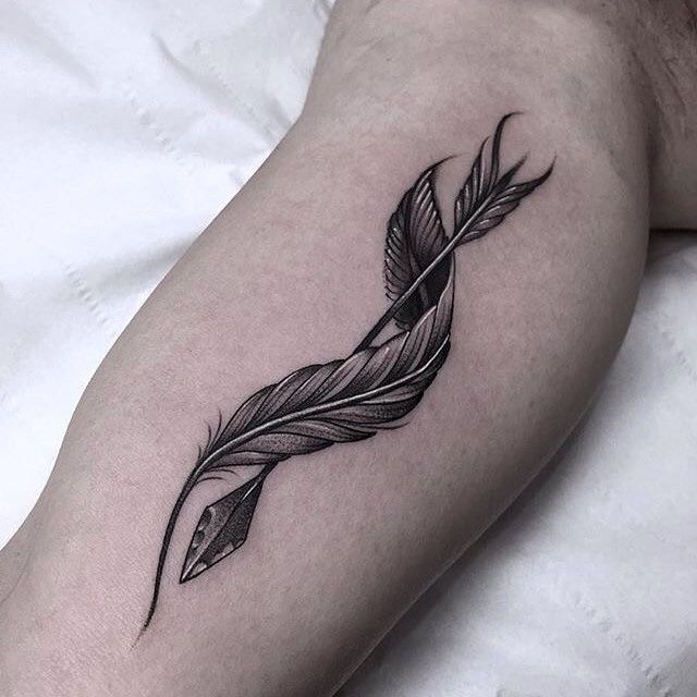 a black and white photo of a feather tattoo on the left thigh, with an arrow in the middle