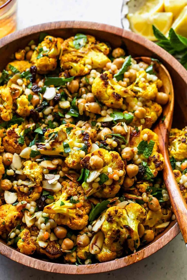 a wooden bowl filled with roasted cauliflower and chickpeas next to a glass of orange juice