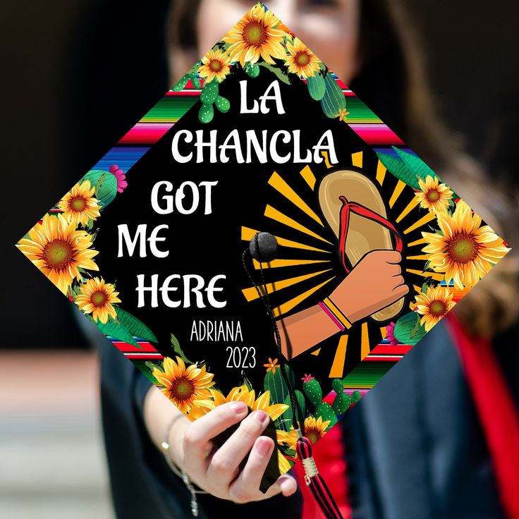 a woman holding a graduation cap that says la chancla got me here and has sunflowers on it