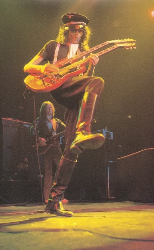 an image of a man that is playing the guitar on stage with his legs in the air