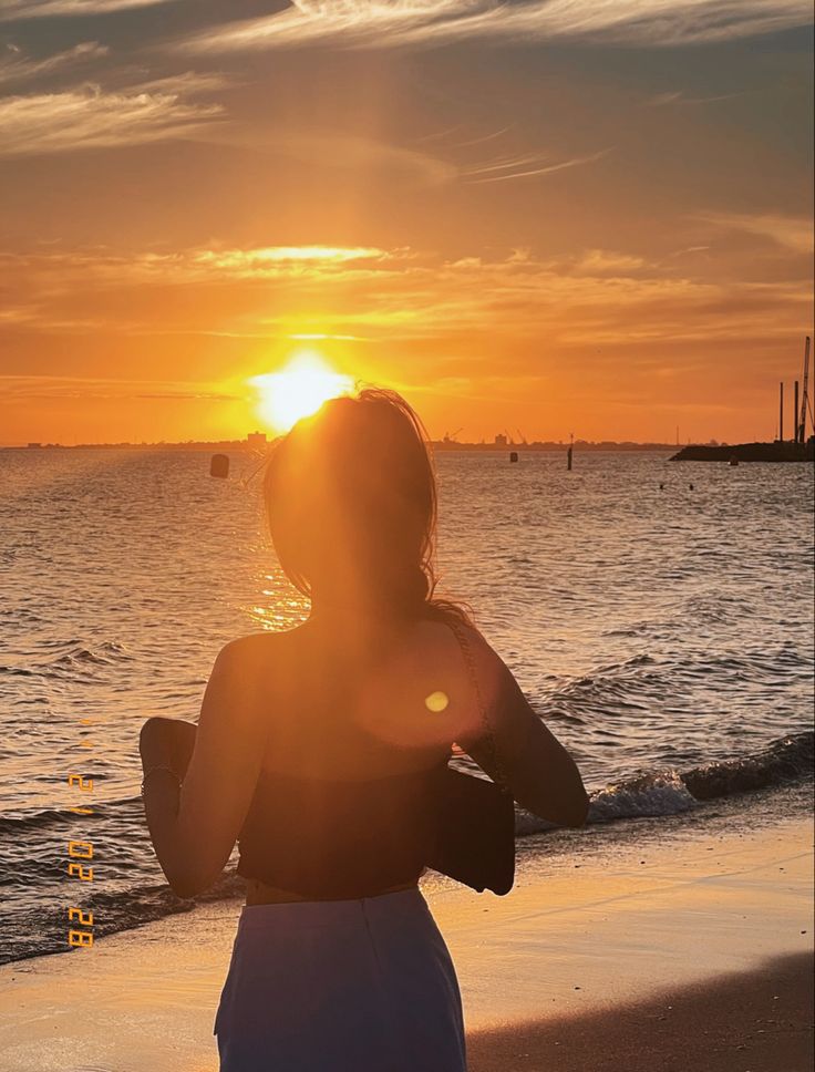 a woman standing on top of a sandy beach next to the ocean at sunset or sunrise