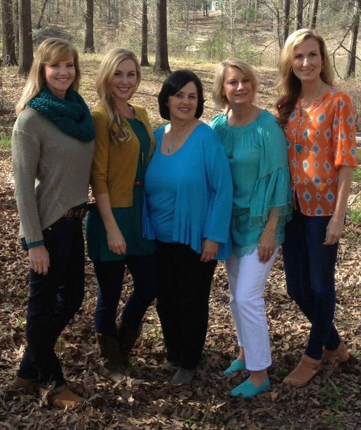 four women standing in the woods posing for a photo with one woman wearing an orange and blue top