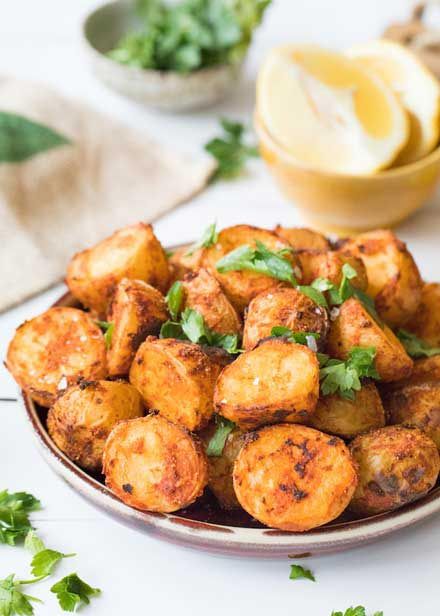 a plate filled with fried potatoes and garnished with parsley next to lemon wedges