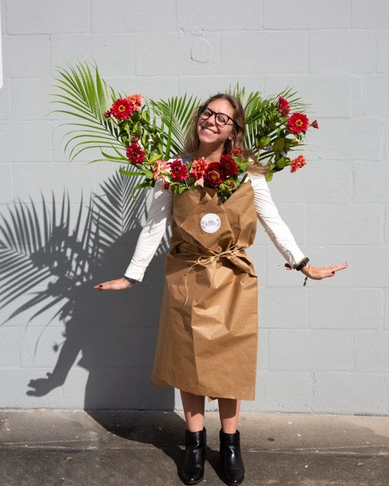 a woman wearing a brown paper bag with flowers on her head and palm leaves behind her