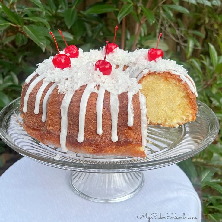 a bundt cake with white icing and cherries on top sitting on a glass plate