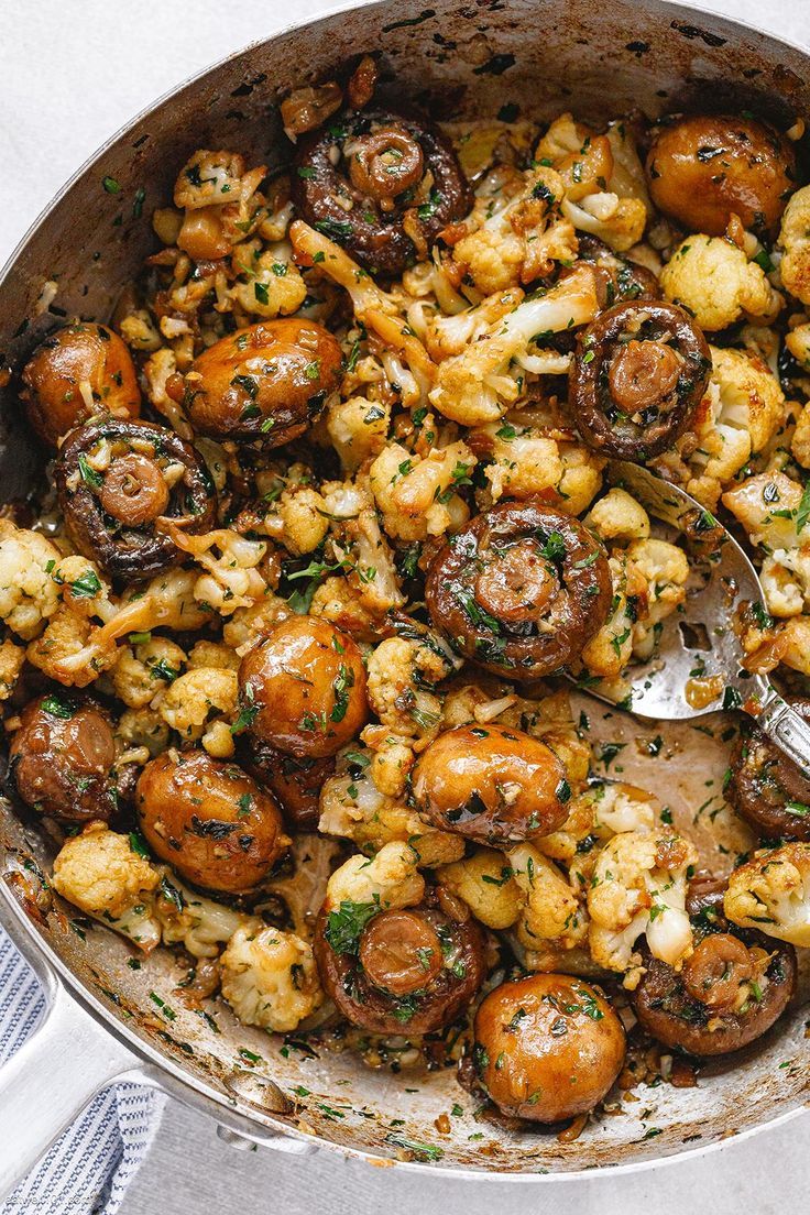 a pan filled with mushrooms and cauliflower on top of a table next to a spoon