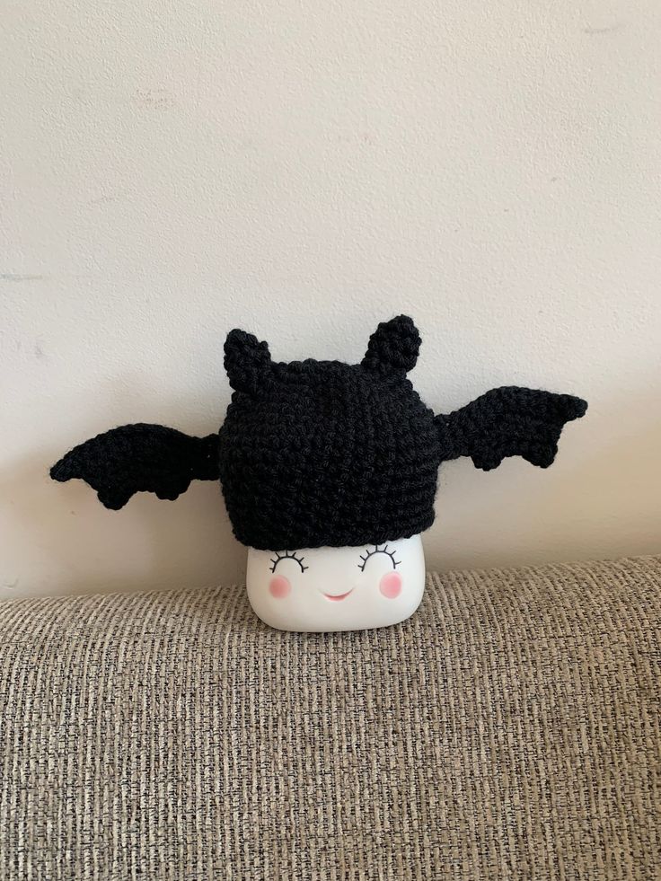 a black knitted bat hat sitting on top of a white headrest with eyes closed