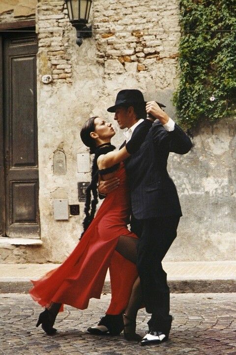 a man and woman are dancing in front of a building with an open door on the side