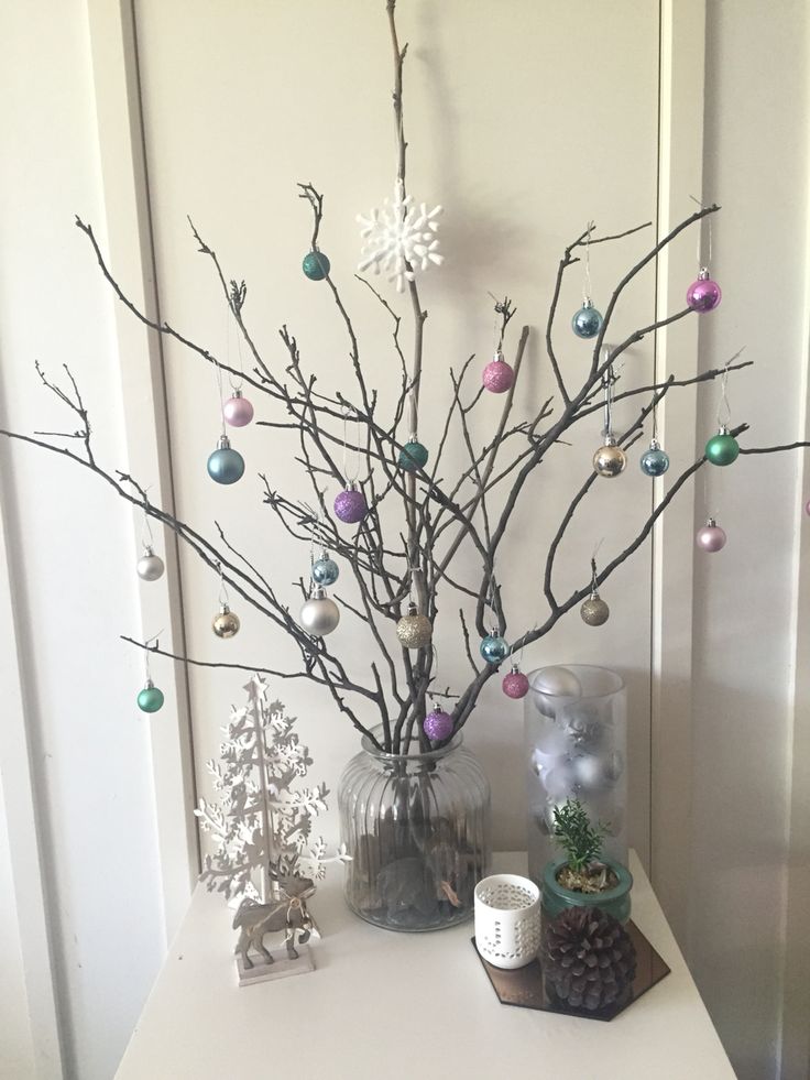 a white table topped with a vase filled with christmas balls and branches covered in ornaments