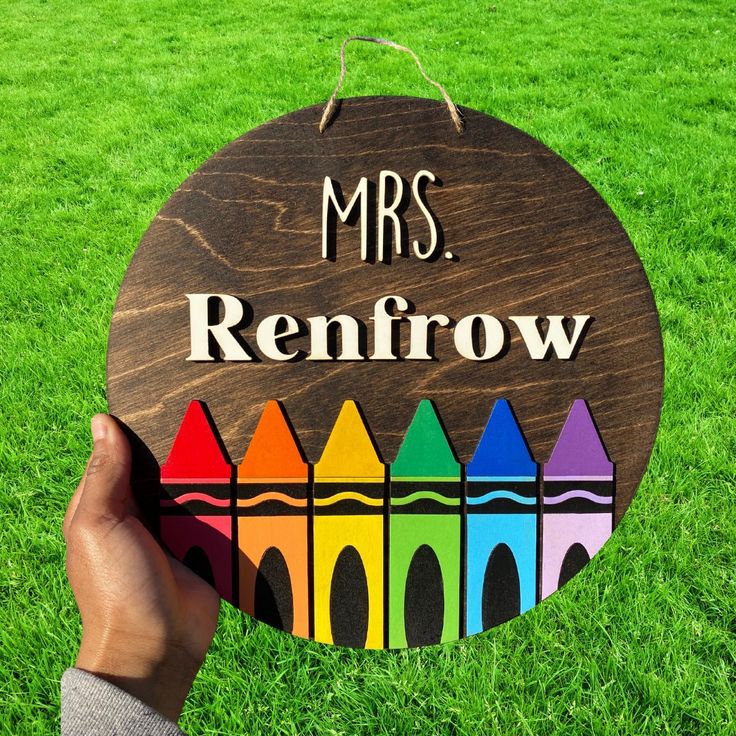 a person holding up a wooden sign with crayons on it that says, mrs renflow