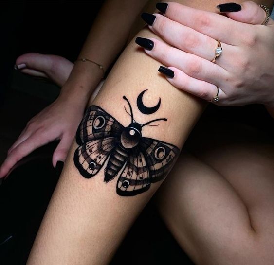 a woman's leg with a butterfly tattoo on it and the moon behind her