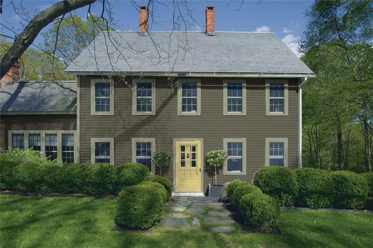 a brown house with yellow door surrounded by green grass and trees in the front yard