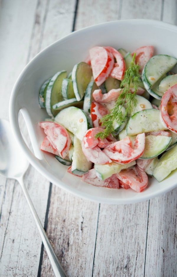 a white bowl filled with cucumbers, tomatoes and other veggies next to a spoon