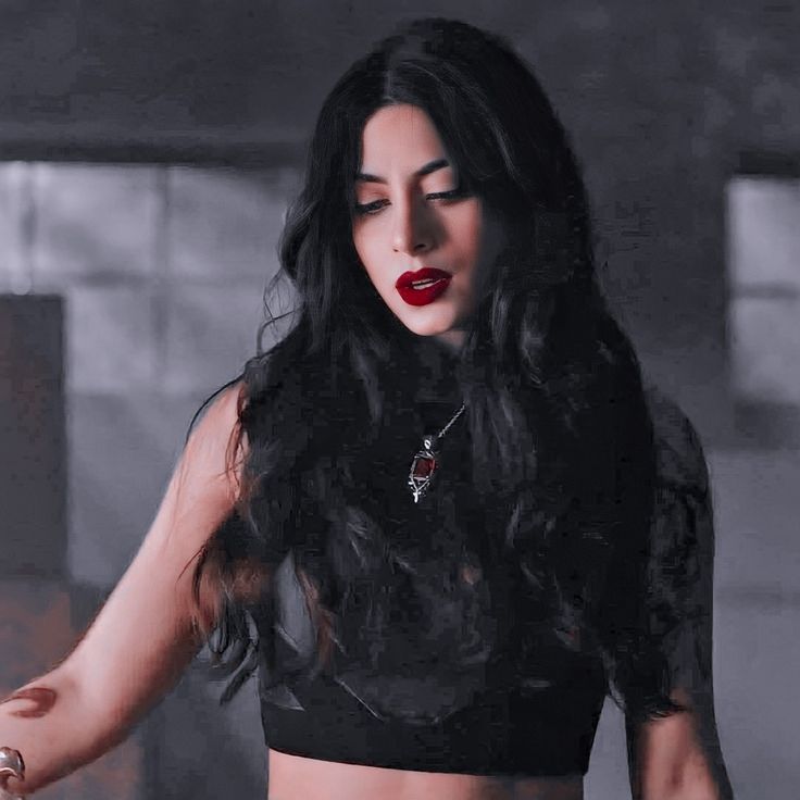 a woman with long dark hair wearing a black top and red lipstick is standing in a dimly lit room