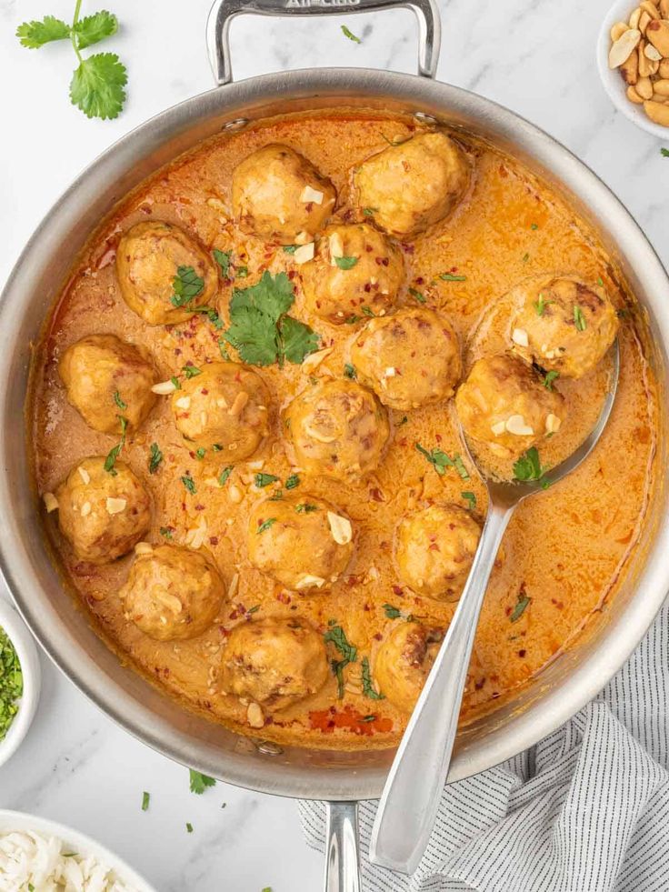 a pan filled with meatballs and sauce on top of a white table next to other dishes