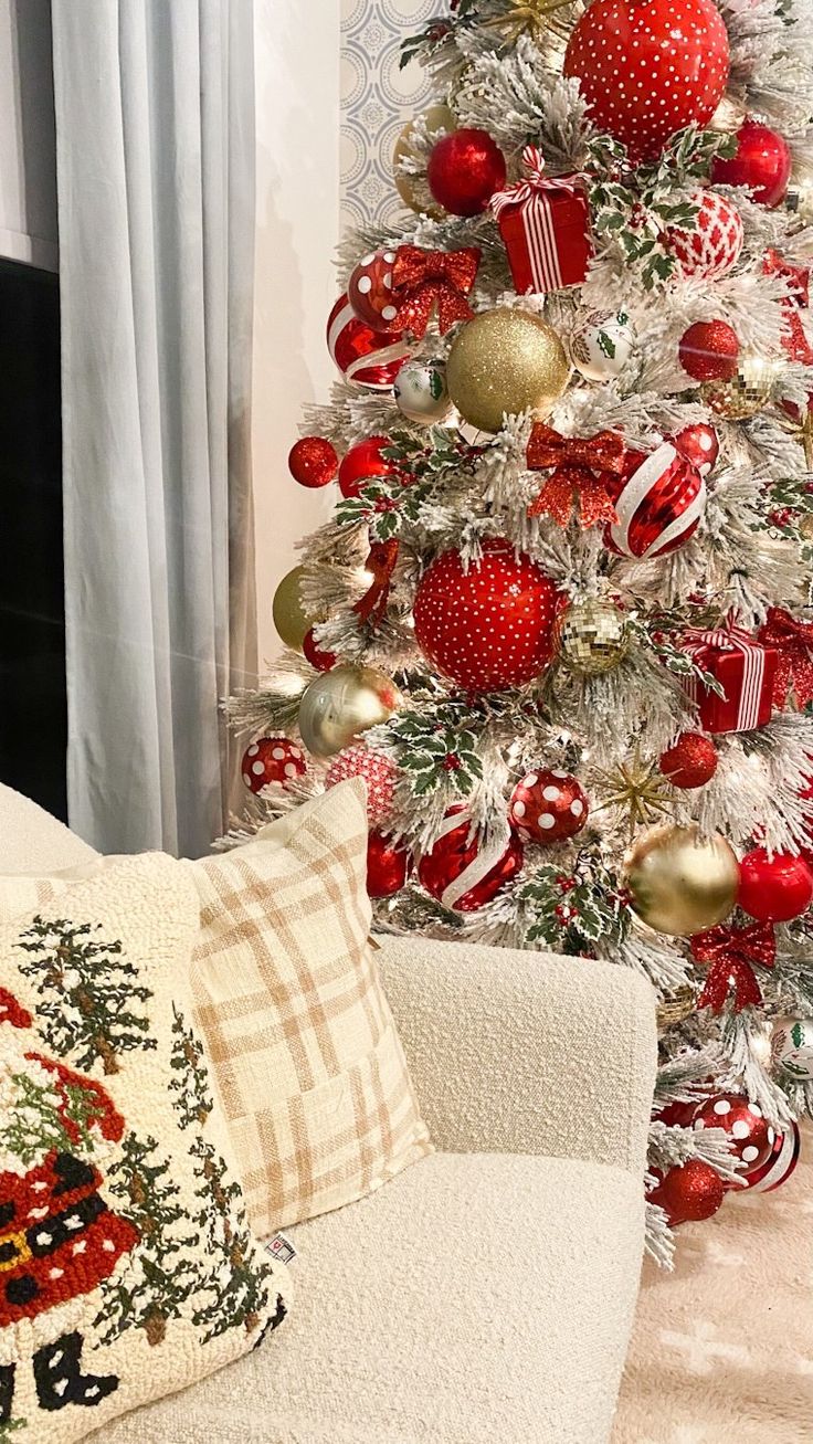 a white christmas tree with red and gold ornaments in the corner next to a couch