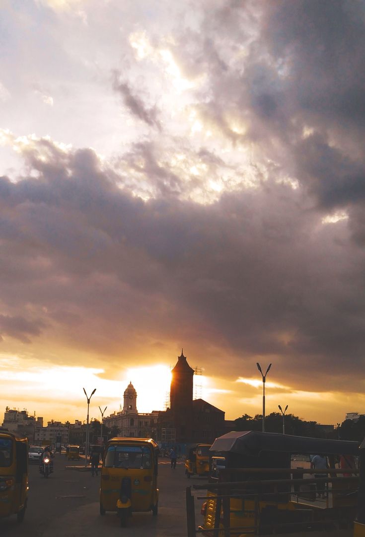 the sun is setting behind some clouds in the sky over a parking lot with cars and trucks