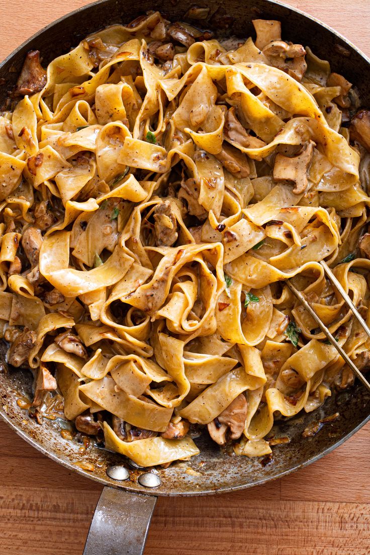 a skillet filled with pasta and meat on top of a wooden table