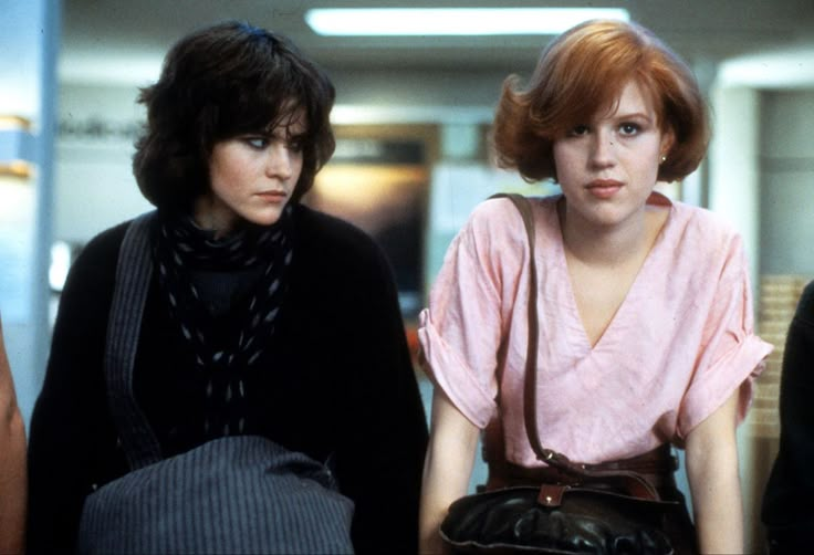 three women standing next to each other in an office building, one wearing a pink blouse