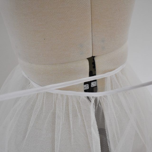 the back of a mannequin wearing a white tulle skirt with a black tie