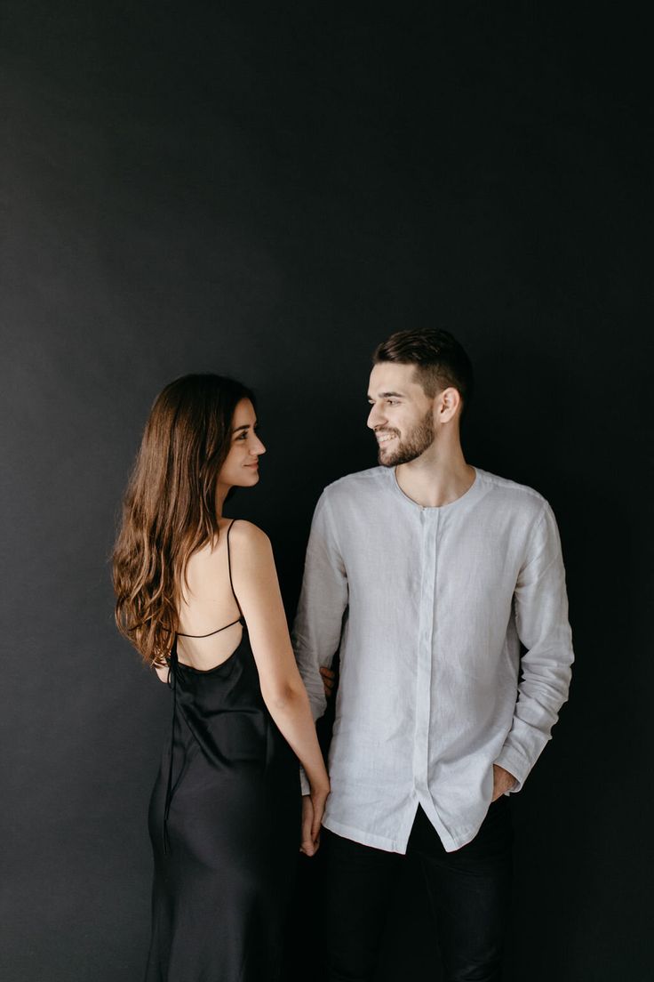 a man and woman standing next to each other in front of a black wall holding hands