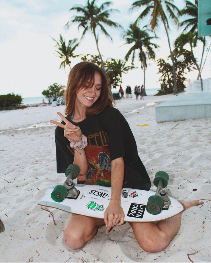 a woman sitting on the beach with a skateboard in her lap and pointing up