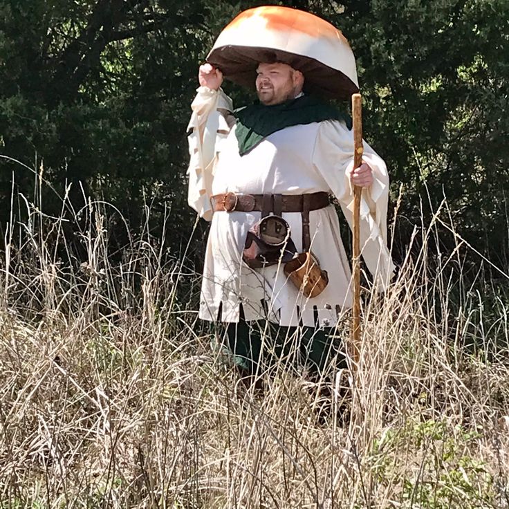 a man dressed in medieval clothing holding a stick and wearing a large hat with an orange on it