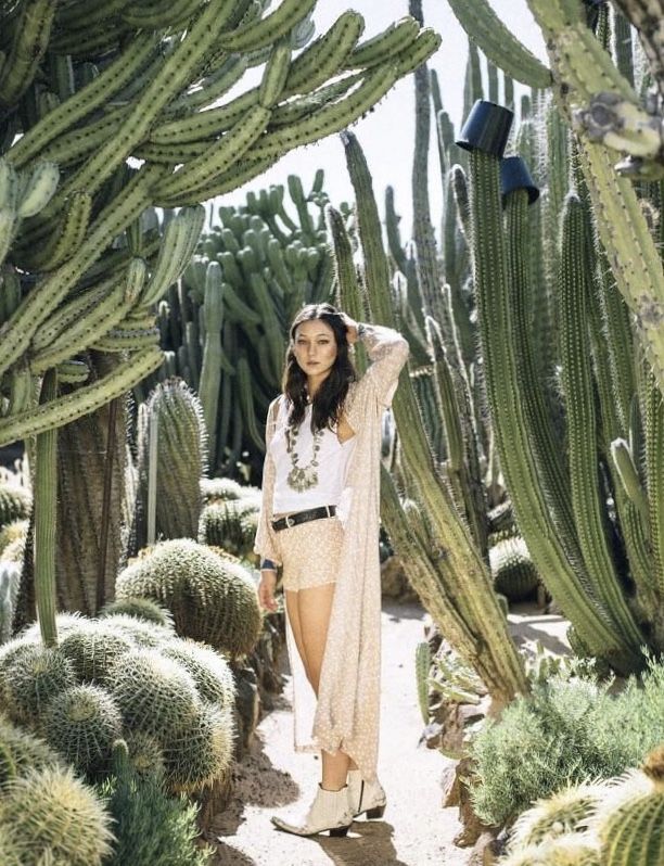 a woman standing in the middle of a desert with cacti and cactus trees