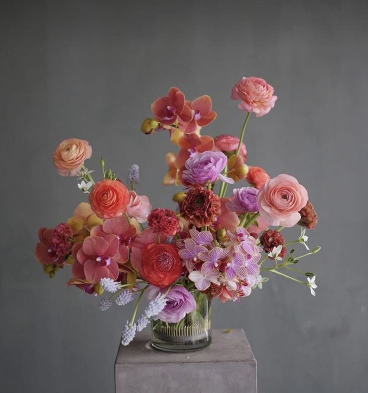 a vase filled with lots of different colored flowers on top of a table next to a gray wall