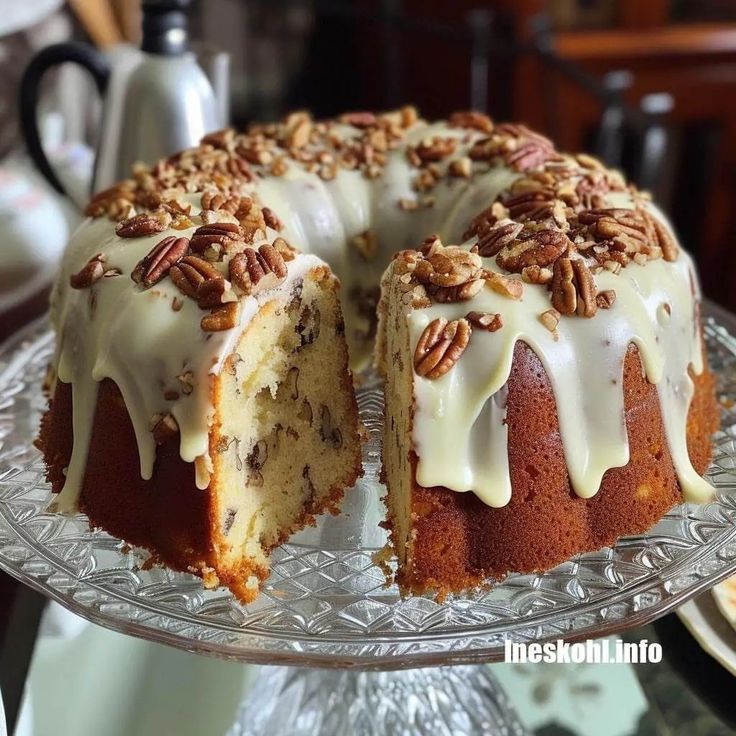 a bundt cake with pecans and icing sitting on a glass platter