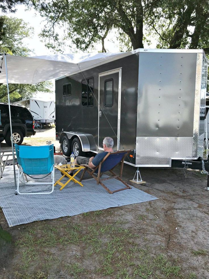 a man sitting in a lawn chair next to a trailer with an awning over it