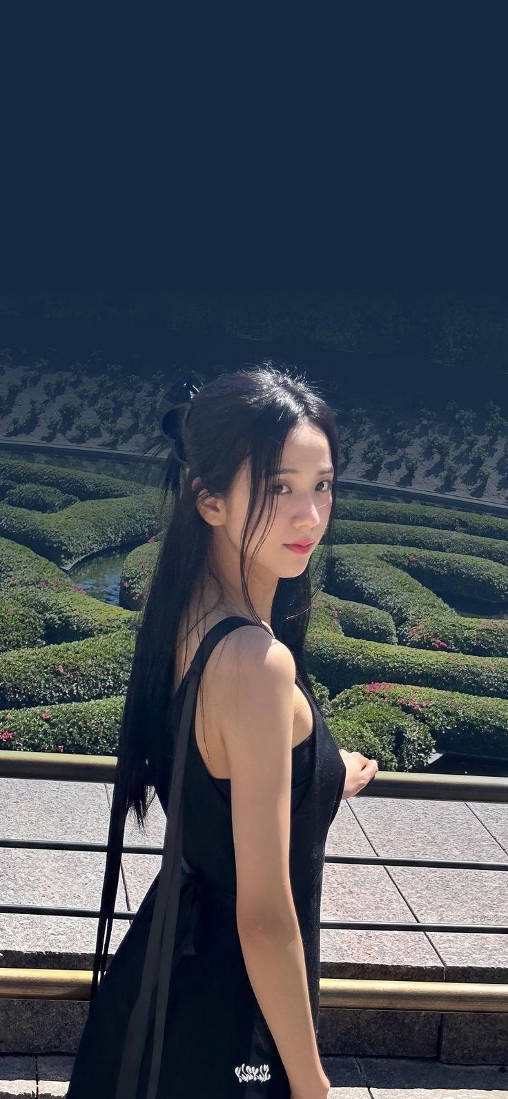 a woman with long black hair is standing in front of a maze and looking at the camera