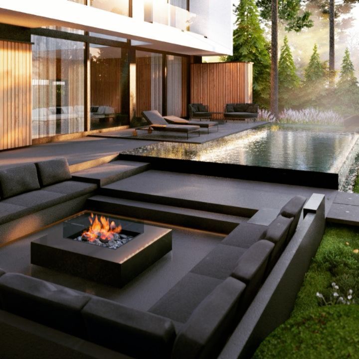 an outdoor living area with couches, fire pit and water feature in the background