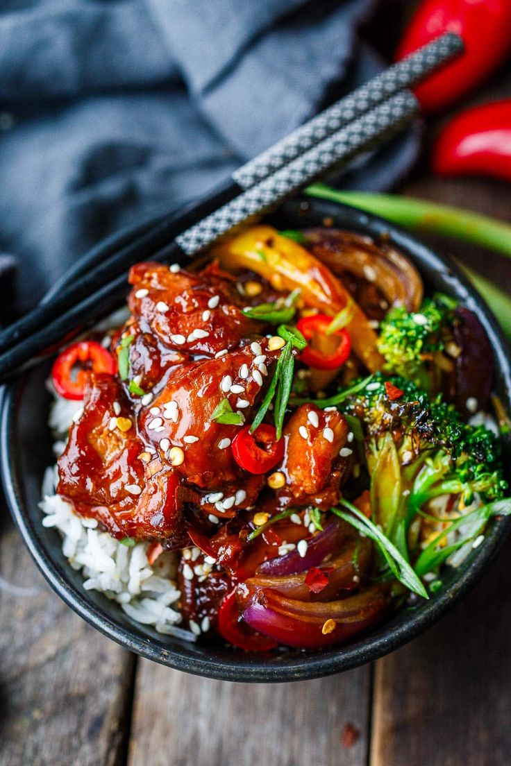 a bowl filled with meat and veggies on top of rice next to chopsticks