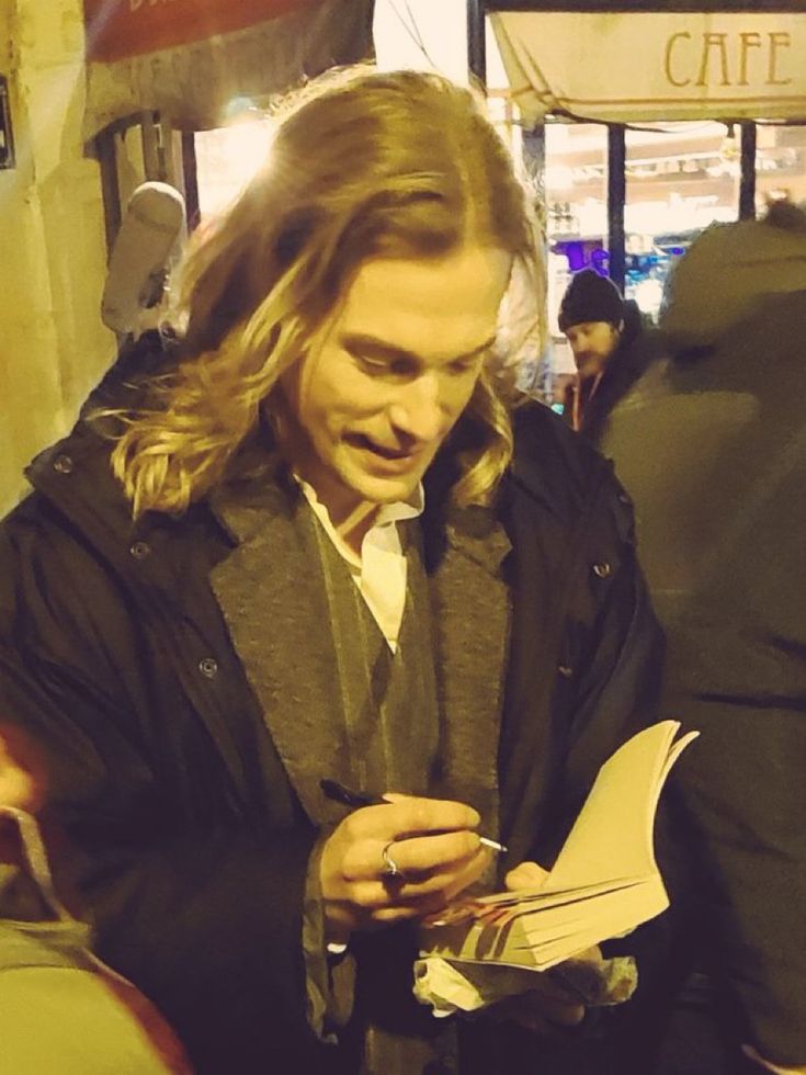 a man with long hair is looking at something in his hand while standing on the street