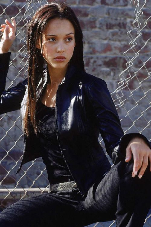 a young woman sitting on the ground next to a chain link fence and looking at the camera