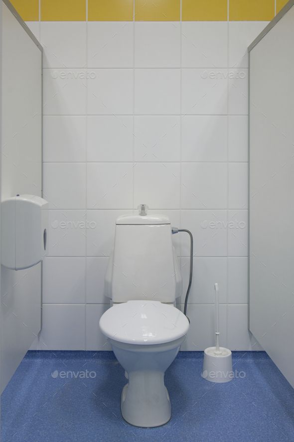 a white toilet sitting in a bathroom next to a trash can and paper dispenser