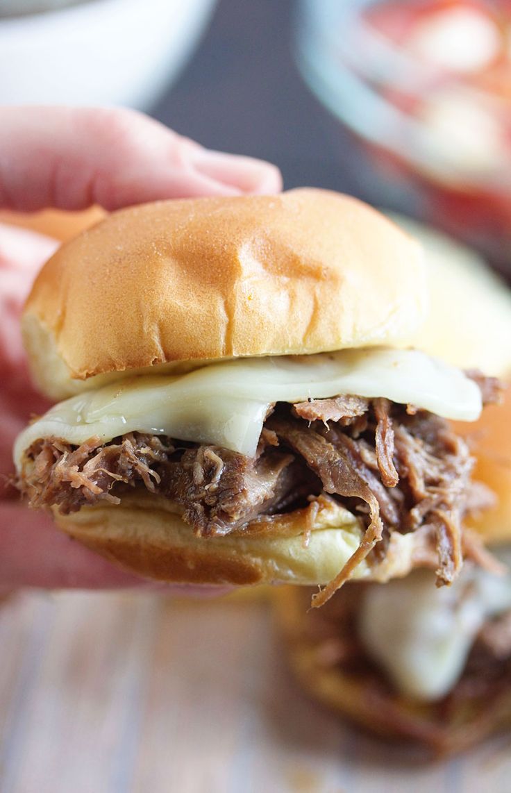 a hand holding a pulled pork sandwich with melted cheese on the top and an egg in the middle