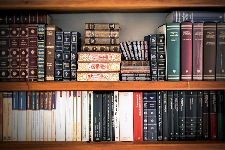 several books are stacked on top of each other in a book shelf with many different colors and sizes