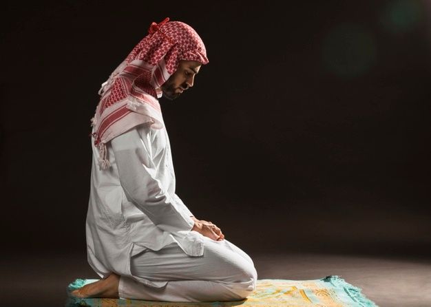 a man sitting on top of a blanket in front of a black background wearing a red and white head scarf